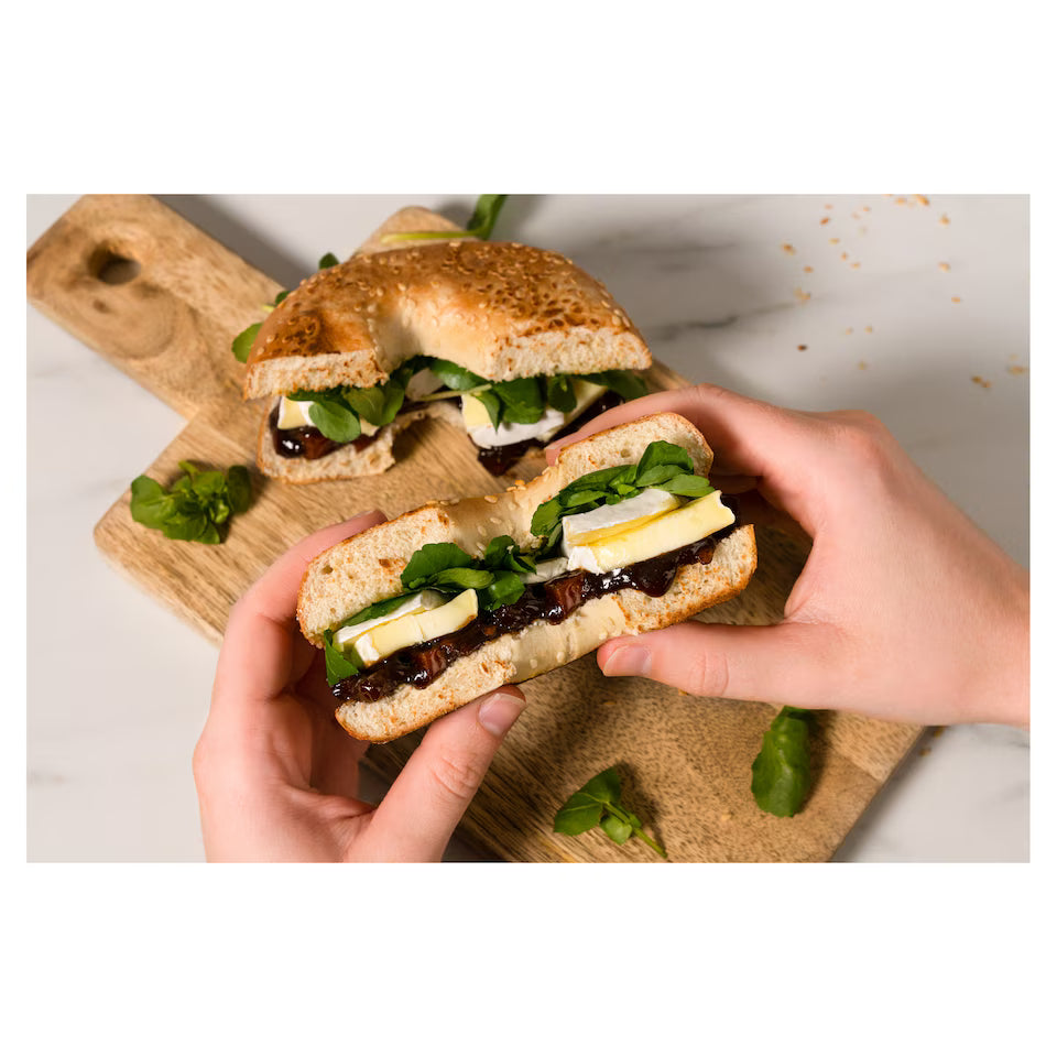 Two hands holding a sandwich with lettuce and cheese on a wooden cutting board.