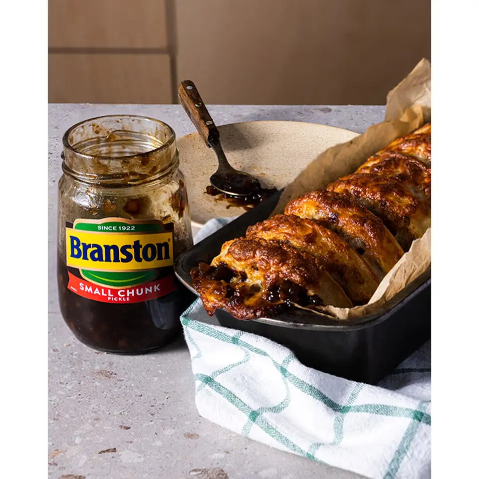 Jar of Branston pickle next to a roasted dish on a table