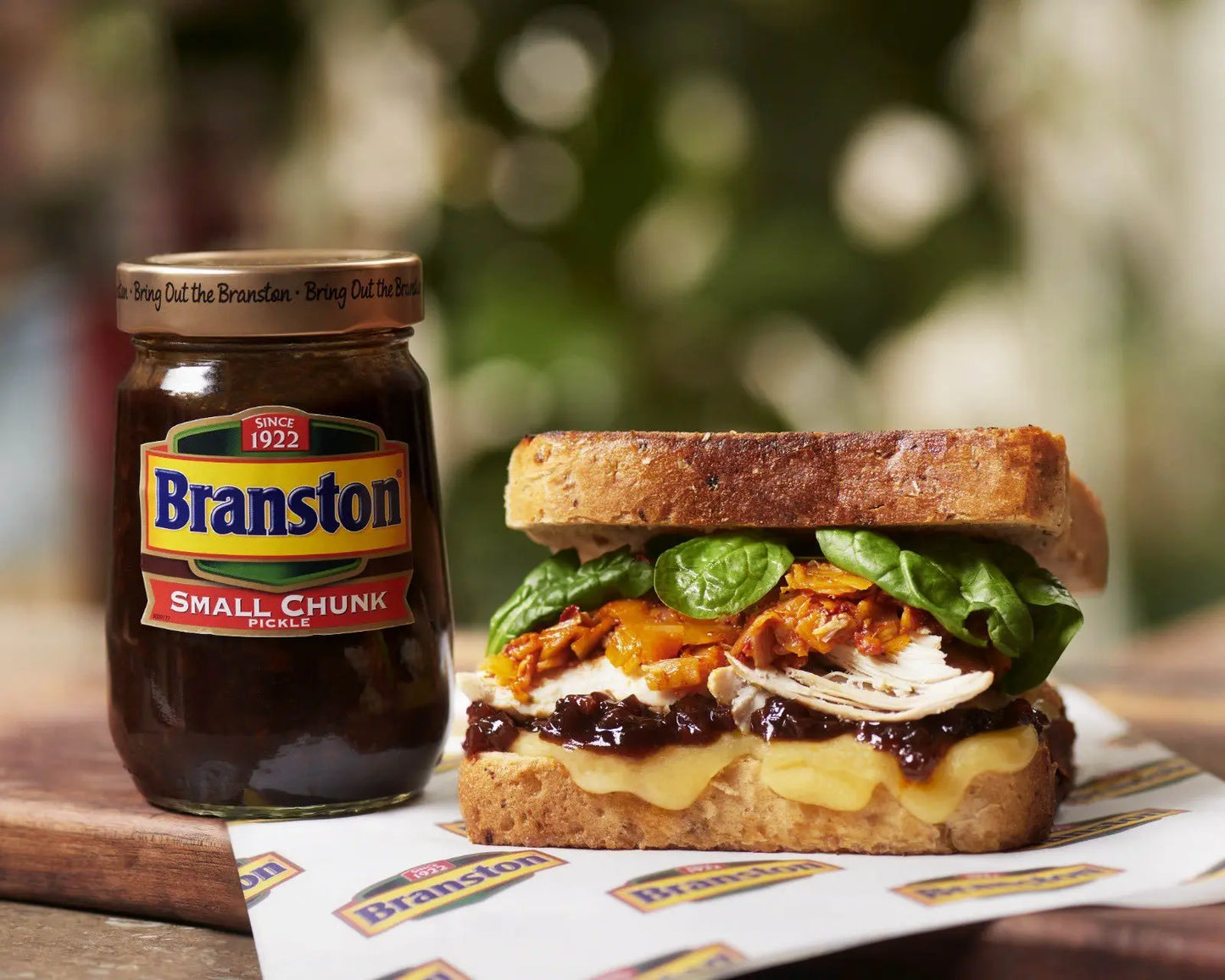 Branston pickle jar next to a sandwich with lettuce and cheese on a wooden board.