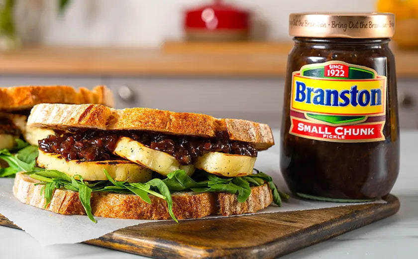 Sandwich with Branston pickle on a wooden board with a jar of Branston pickle in the background.