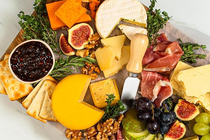 Assorted cheese plate with fruits, meats, and crackers on a wooden board.