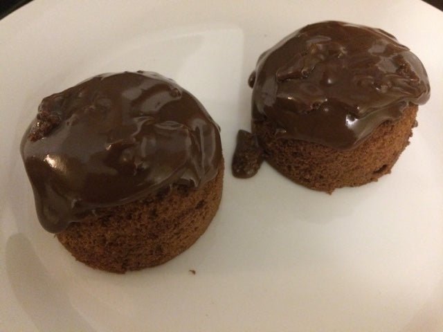 Two chocolate cupcakes with a glossy glaze on a white plate.