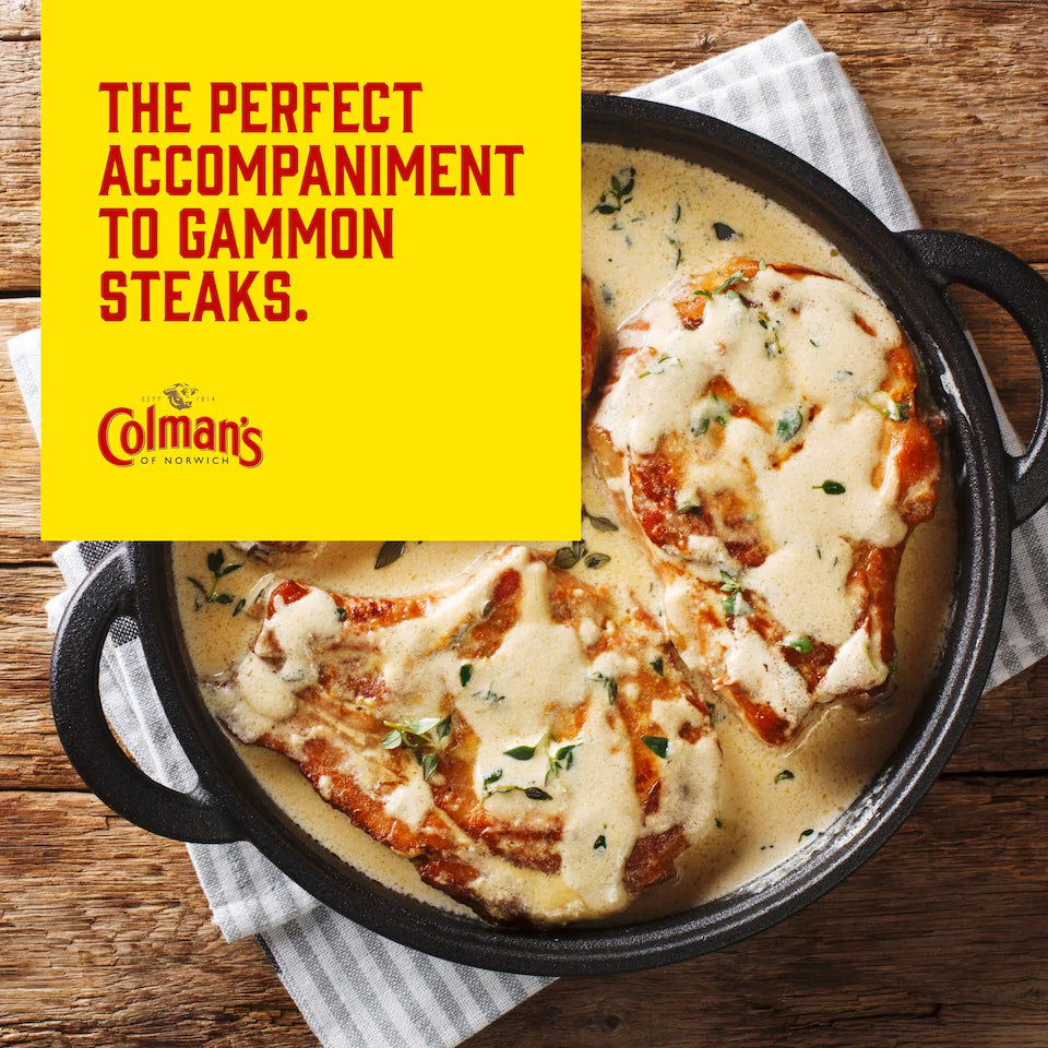 Colman's gammon steaks with creamy sauce in a pan on a wooden surface.