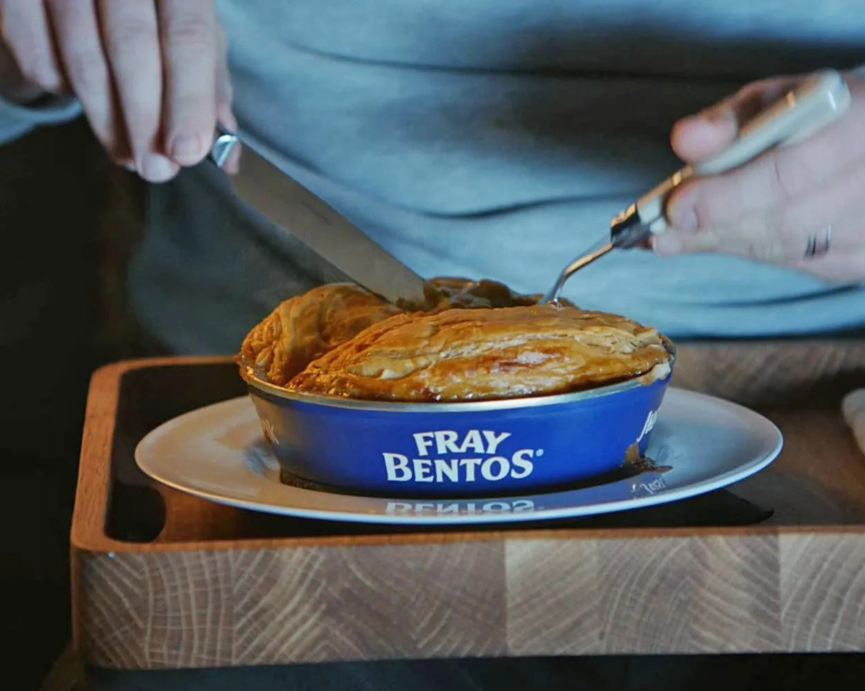 Person cutting into a pie in a Fray Bentos container on a wooden table