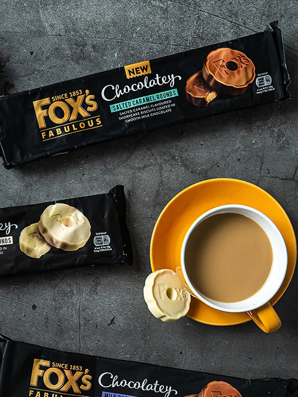 Fox's Fabulous chocolate buns packaging with a cup of coffee on a dark surface