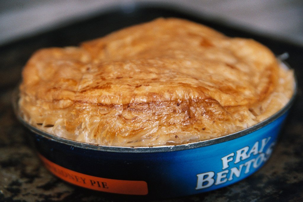 Pasty in a blue Fray Bentos container on a dark surface