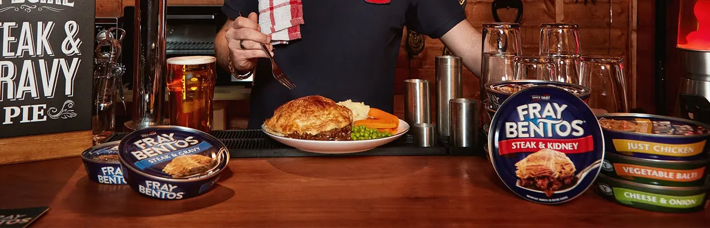 Person at a bar with a plate of food and Fray Bentos products on the counter.
