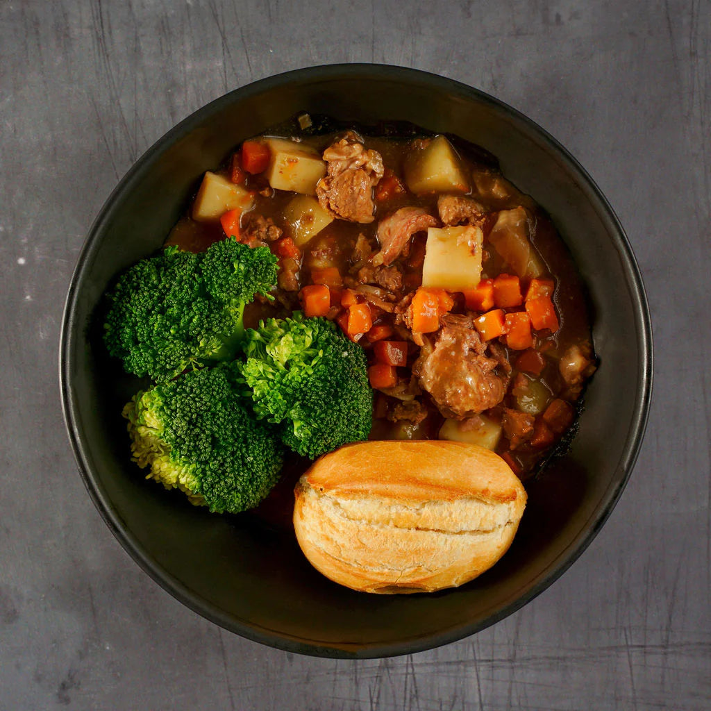 Bowl of stew with vegetables and a roll on a gray background