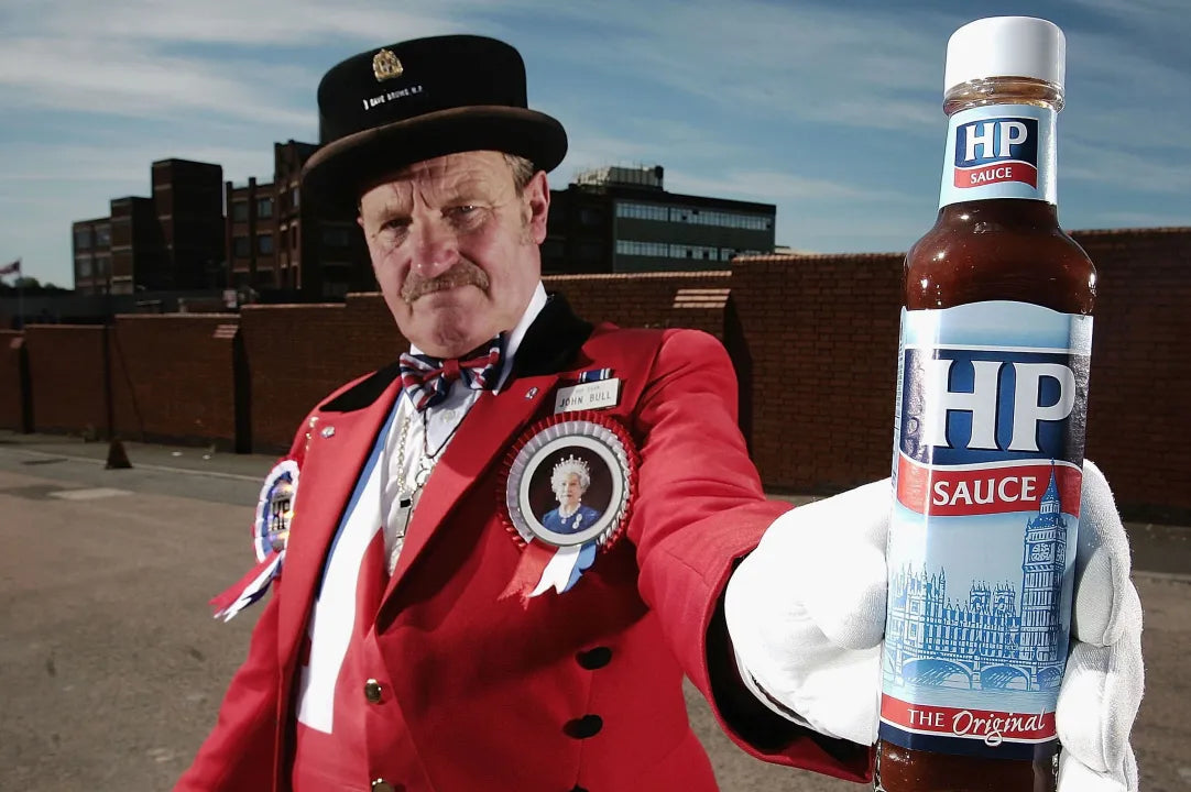 Person in a red uniform holding an HP sauce bottle outdoors.