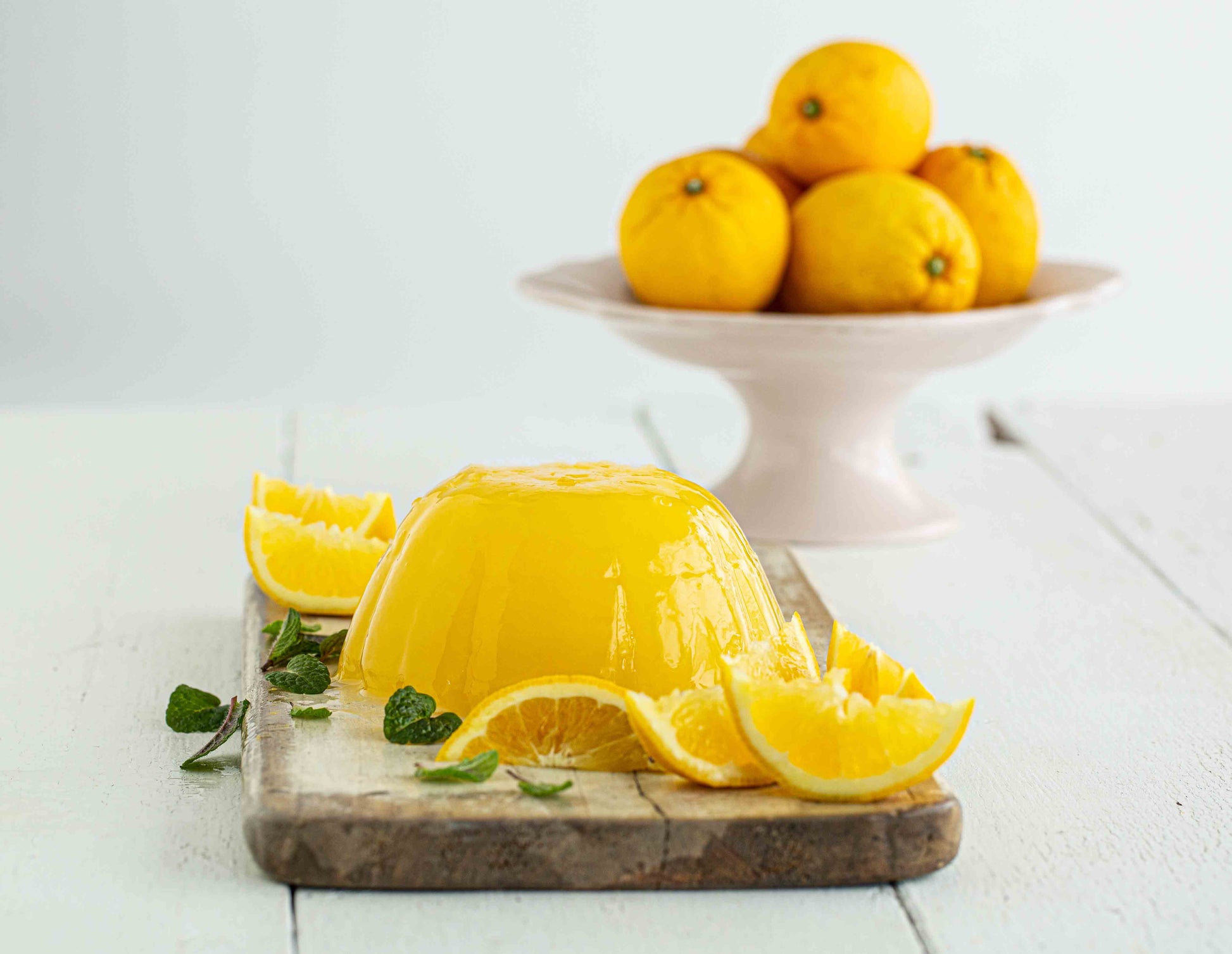 Yellow jelly dessert with lemon slices on a wooden board, lemons in the background.