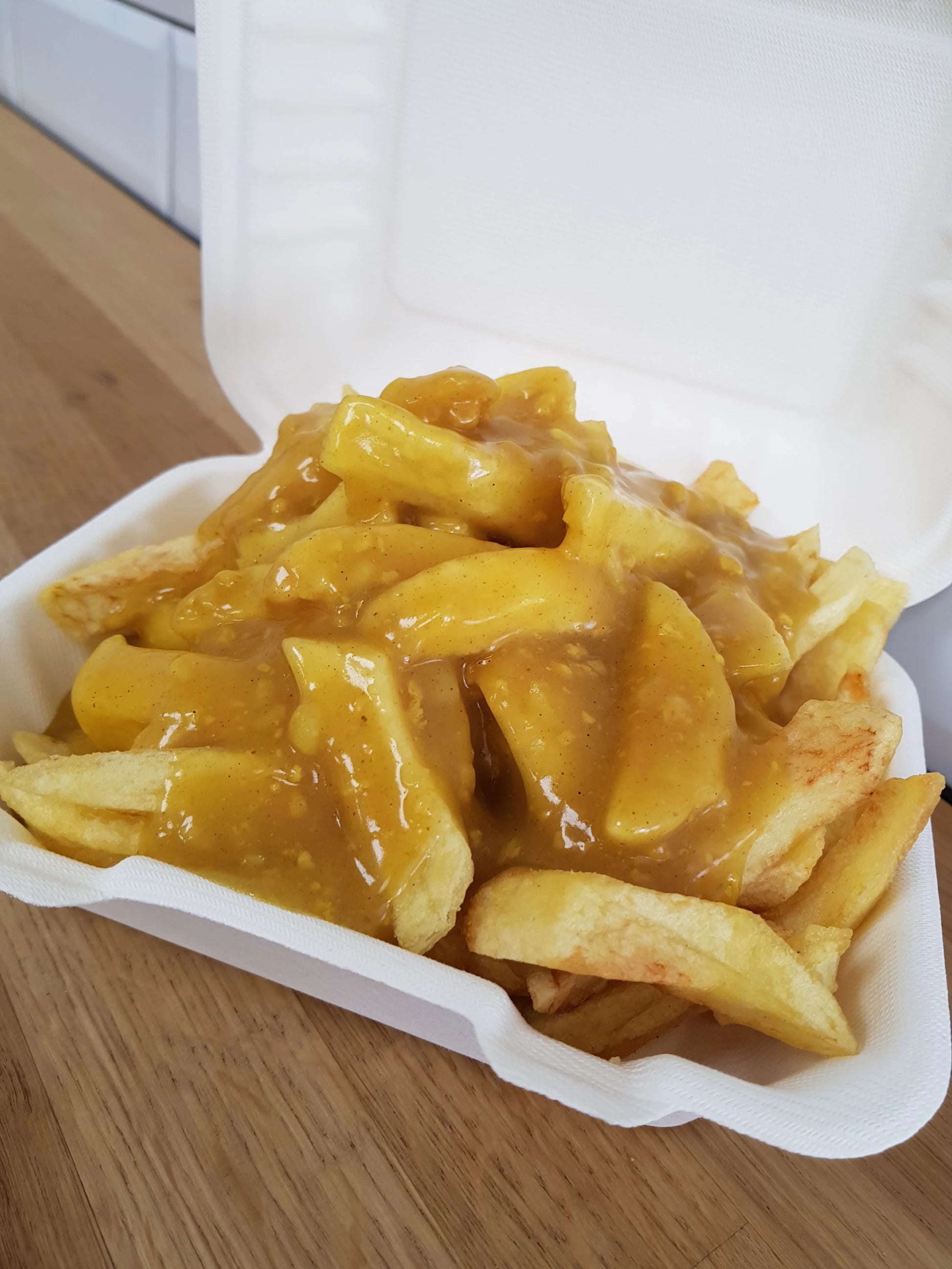 French fries with a yellow sauce in a white container on a wooden surface