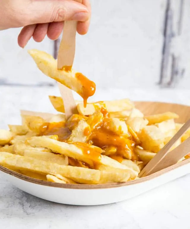 Fries being dipped into a bowl of caramel sauce with a wooden spoon.
