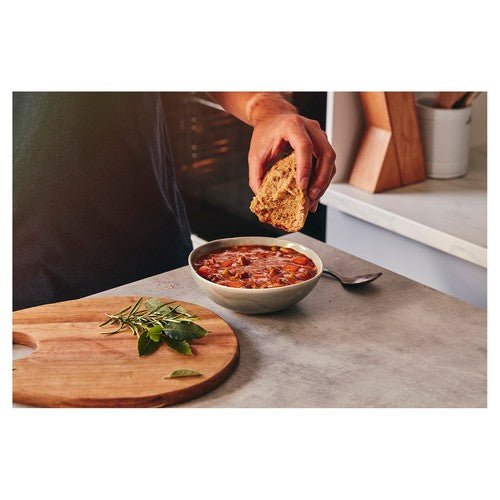 Person dipping bread into a bowl of soup on a kitchen counter.