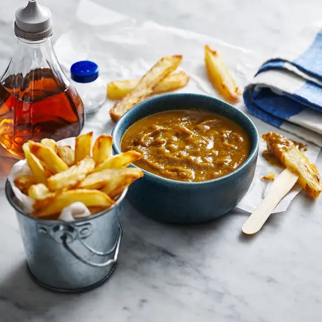 Fries in a metal bucket with a bowl of dipping sauce on a marble surface.