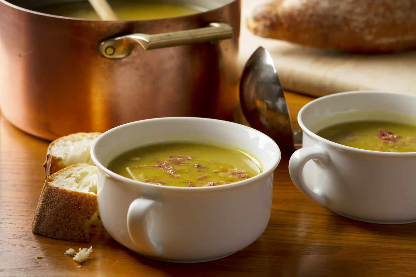 Two bowls of soup on a wooden table with bread slices.