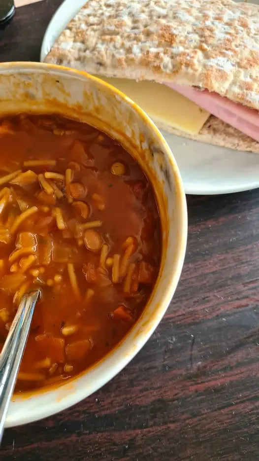 Bowl of soup with a sandwich in the background on a wooden table