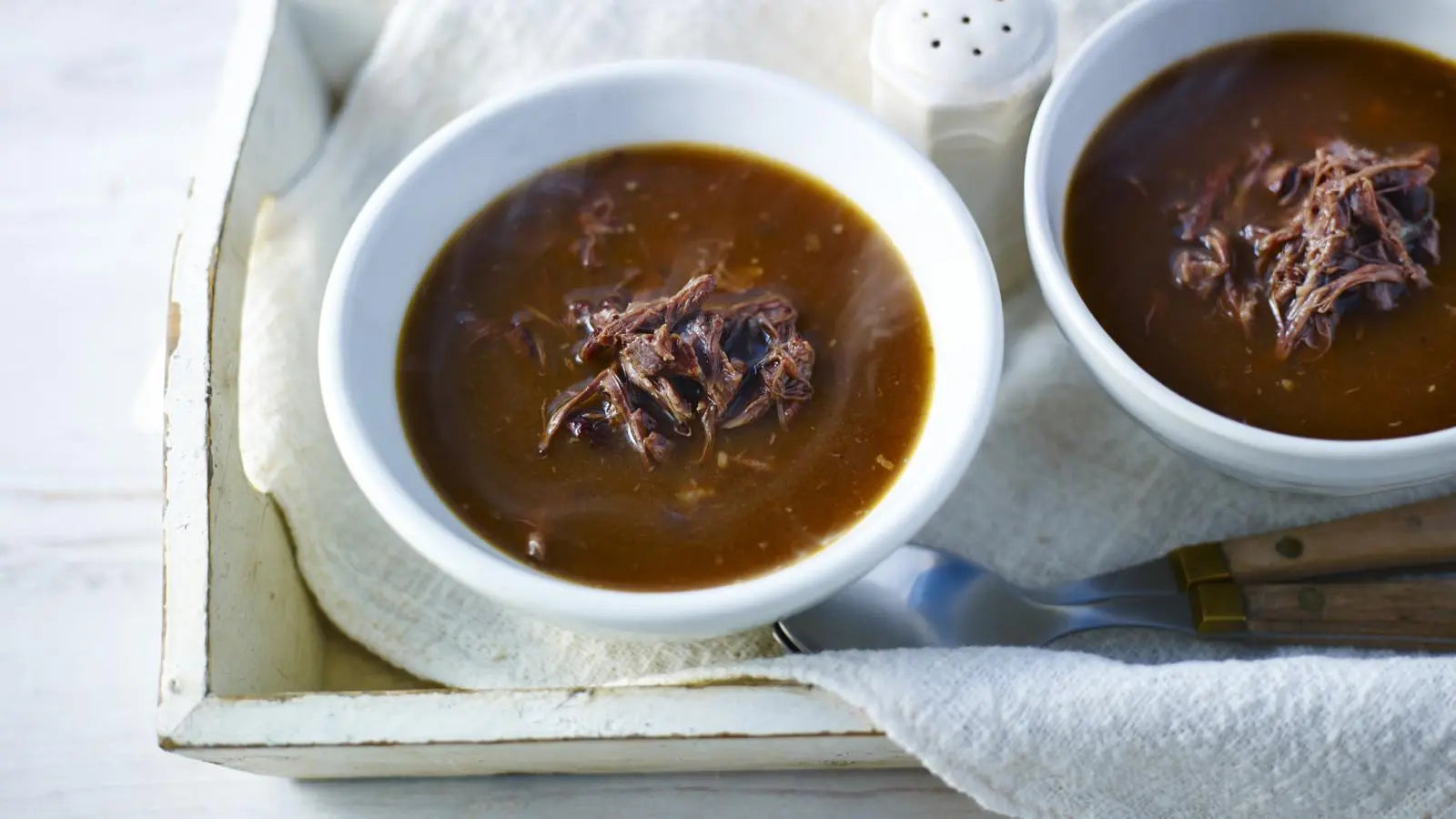 Two bowls of oxtail soup with meat on a white cloth