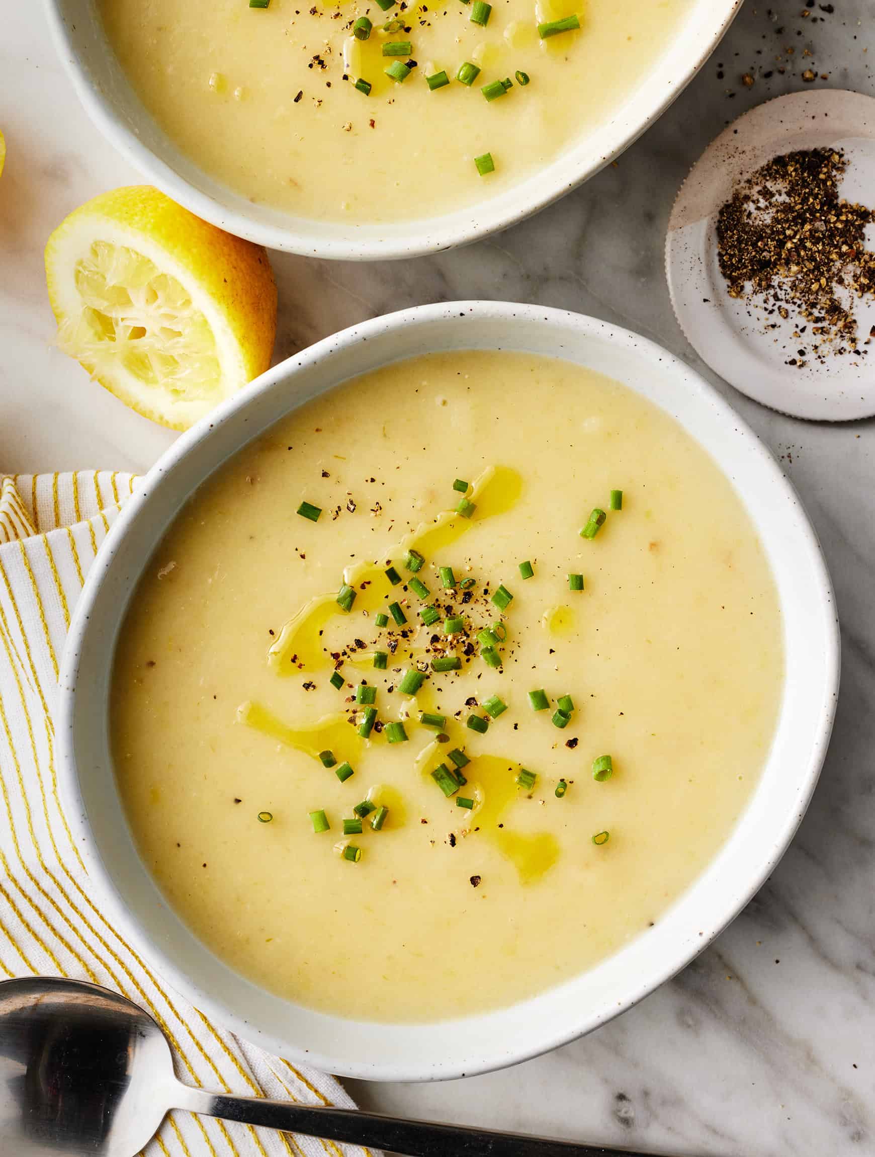 Bowl of potato and leek soup with garnish on a marble surface.