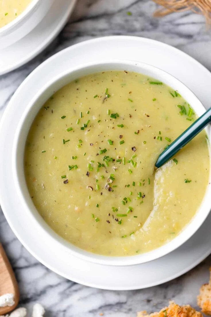 White bowl of potato and leek creamy soup with a spoon on a marble surface