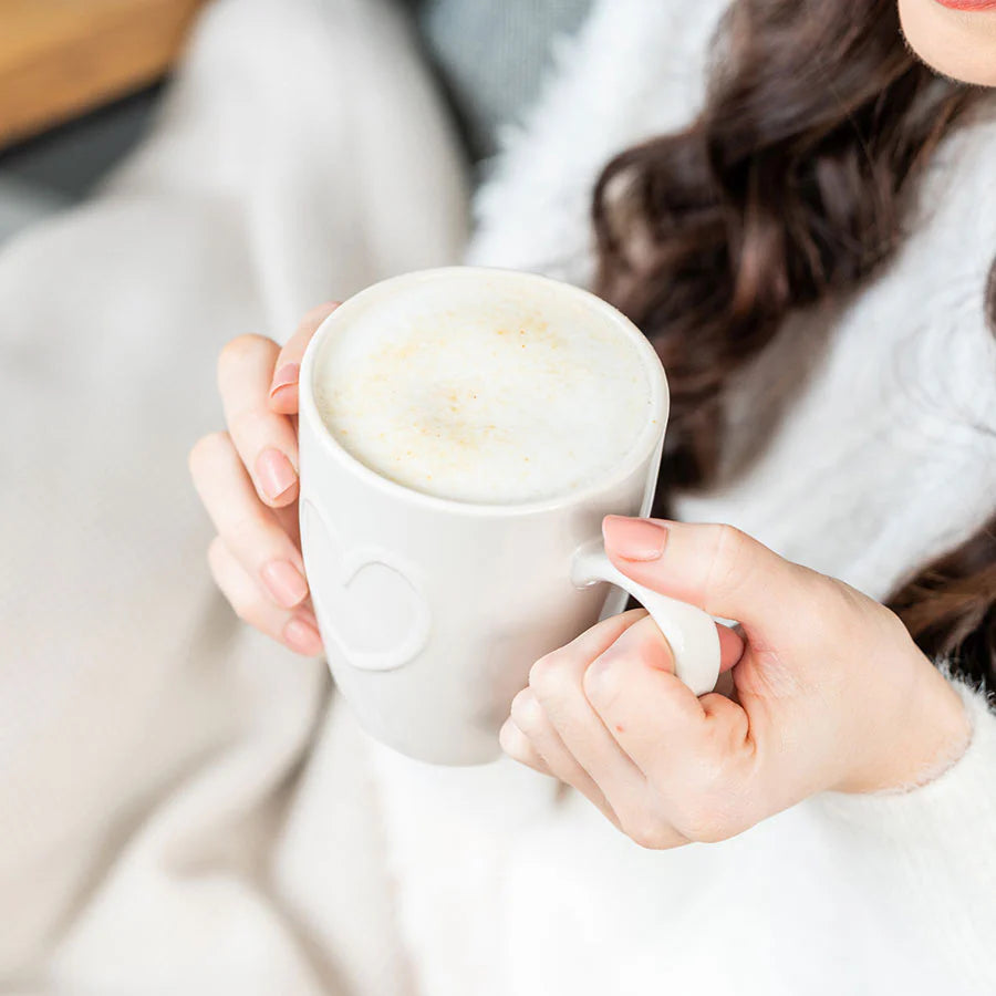 Person holding a white mug with Horlicks warm beverage, in a cozy setting.