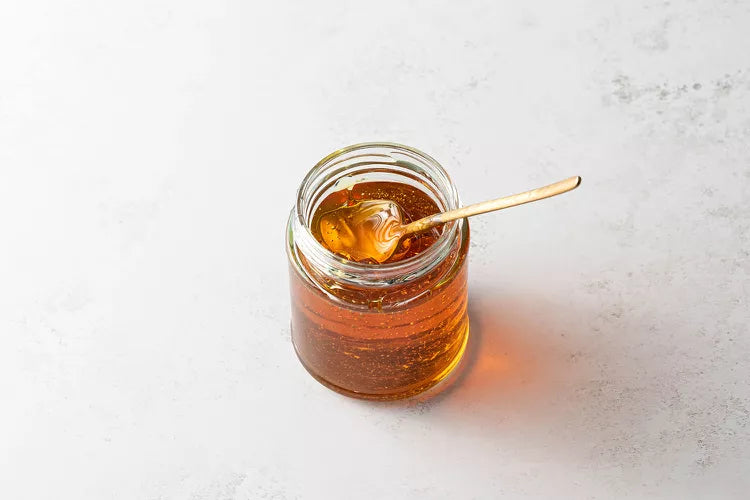 Jar of honey with a honey dipper on a light gray background
