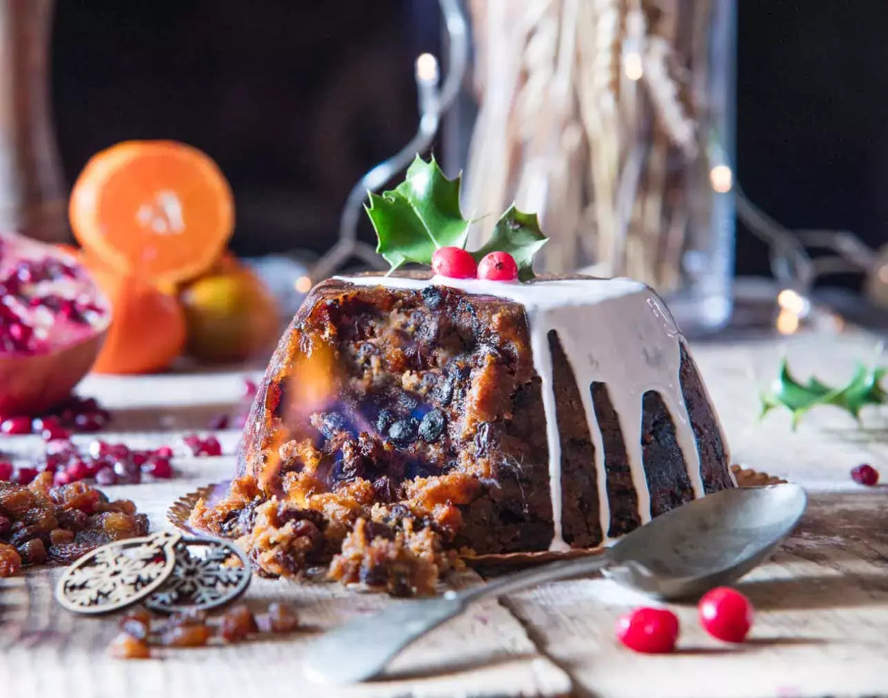 Christmas pudding with whipped cream, holly leaves, and red berries on a wooden table.