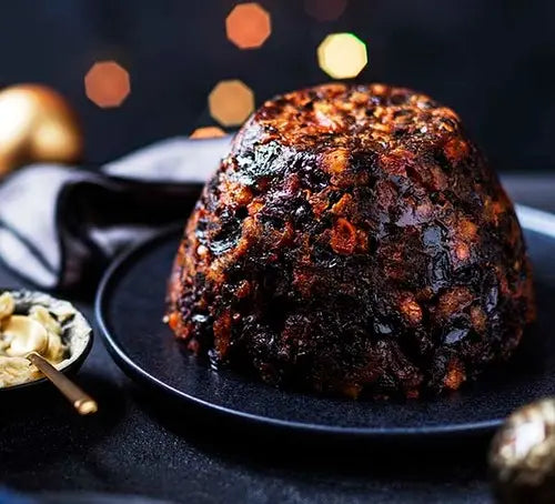 Christmas pudding on a black plate with festive lights in the background