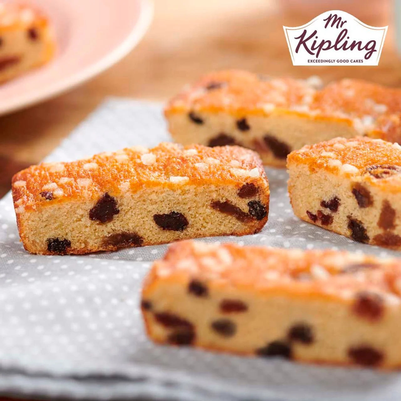 Slices of cake with raisins on a gray surface, branded with 'Mr Kipling'.
