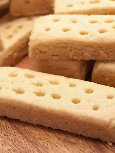 Close-up of several rectangular biscotti cookies stacked on a wooden surface. The cookies are light tan with small circular holes running along the top.