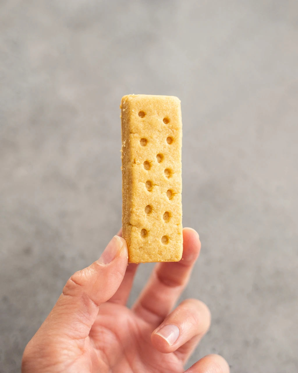 Hand holding a Paterson's Clotted Cream Shortbread with holes against a gray background