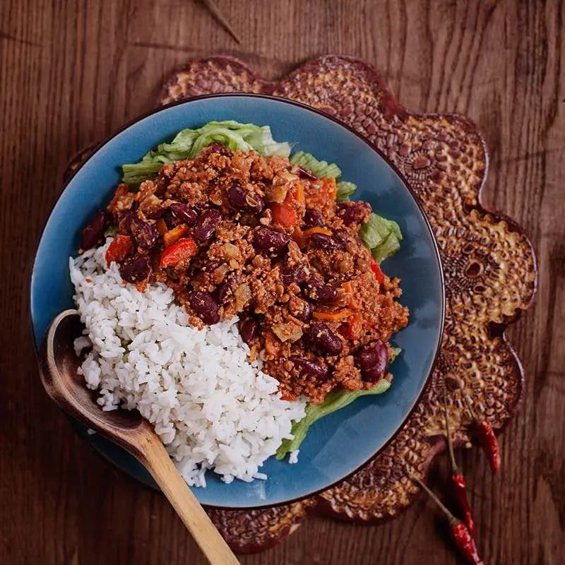 Blue plate with rice, beans, and Schwartz Chili Con Carne on a wooden surface