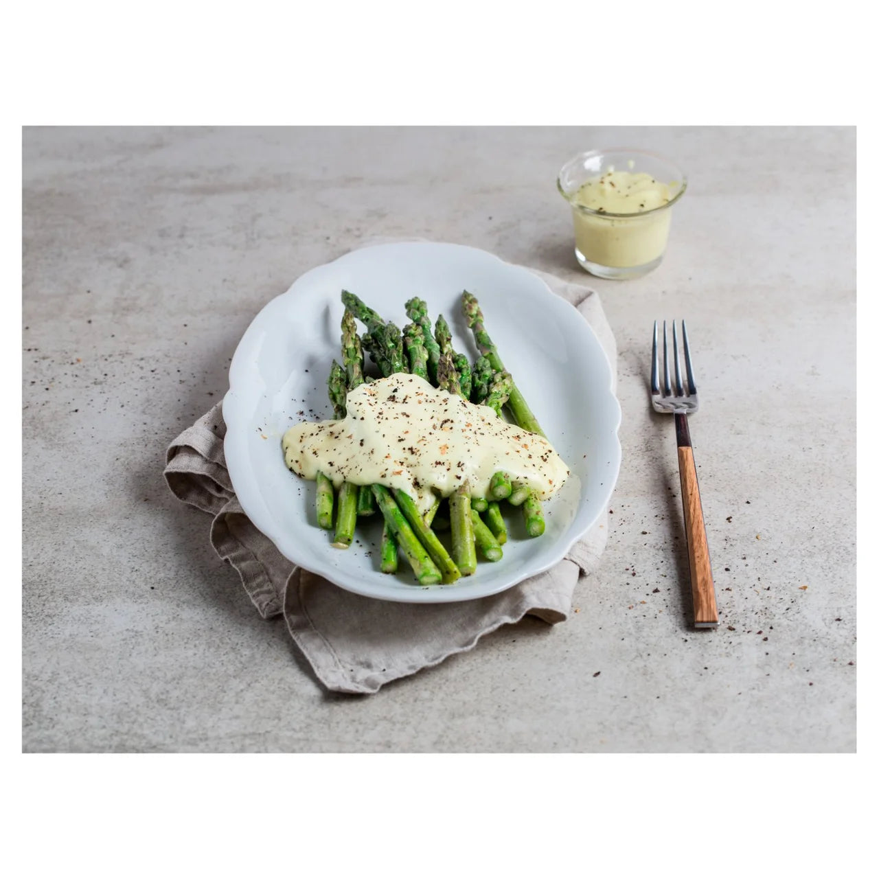 Plate of asparagus with a creamy sauce on a textured surface with a glass of water and fork.