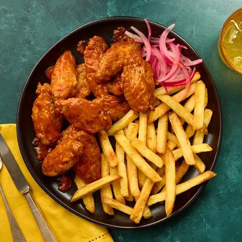Platter of Schwartz Honey Chilli Chicken wings with French fries and pickled onions on a dark plate.