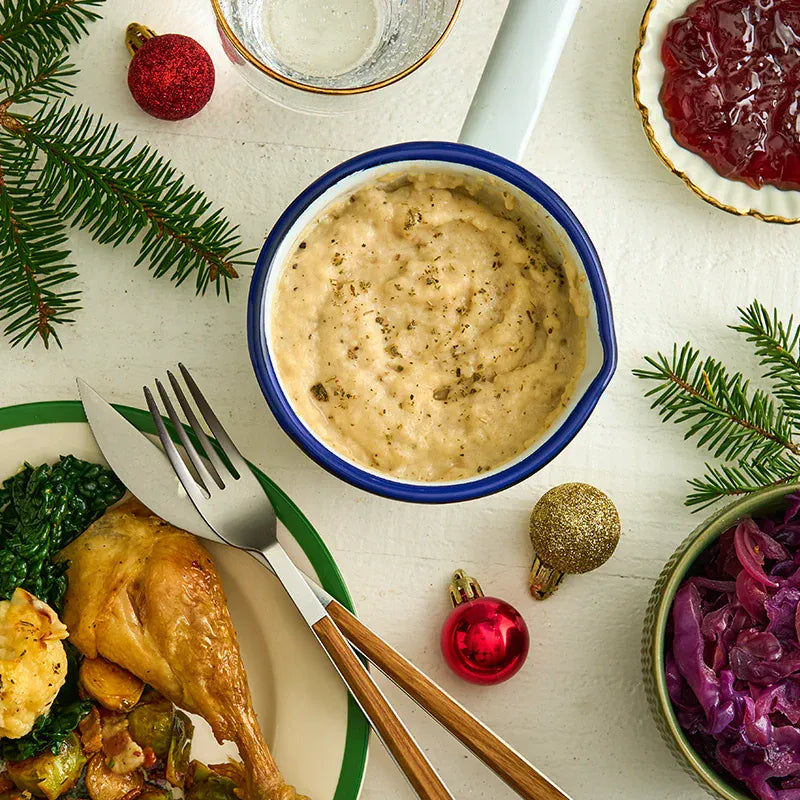 Bowl of Schwartz Luxury Bread Sauce on a plate with roasted chicken and vegetables, surrounded by Christmas decorations.