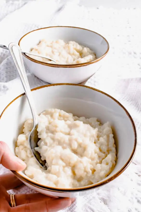 Person holding a bowl of rice pudding with a spoon, placed on a white surface.