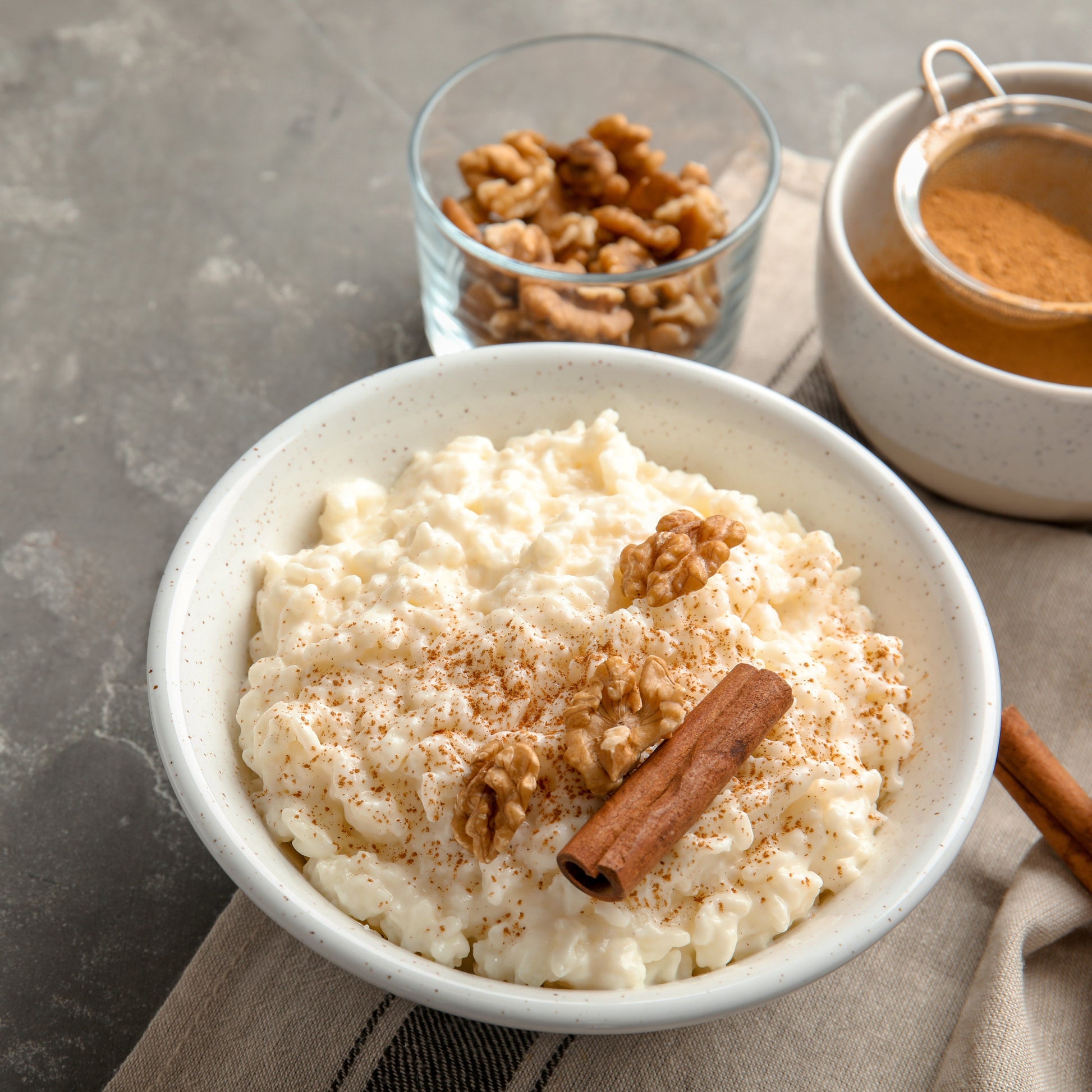 Bowl of rice pudding with cinnamon and walnuts on a gray surface