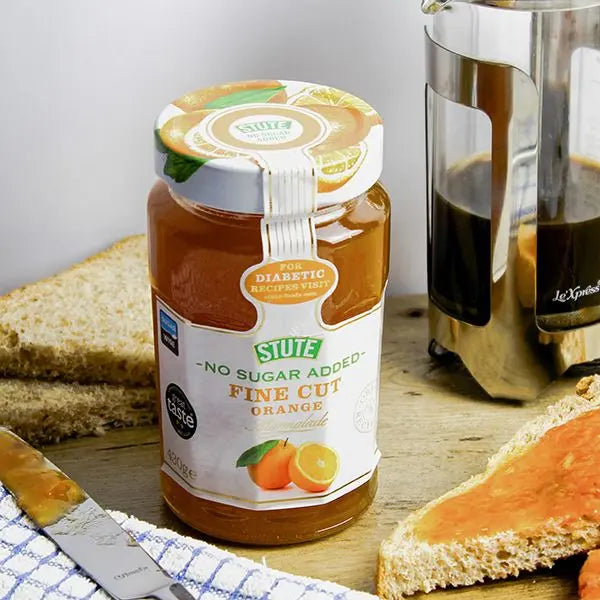 Jar of Stute No Sugar Added Fine Cut Orange Jam on a table with toast and coffee.