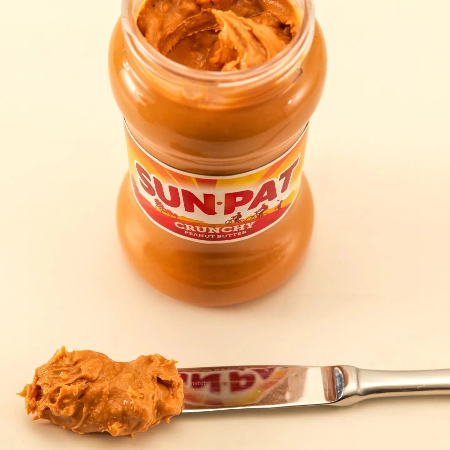 Jar of Sun-Pak crunchy peanut butter with a spoonful on a beige background