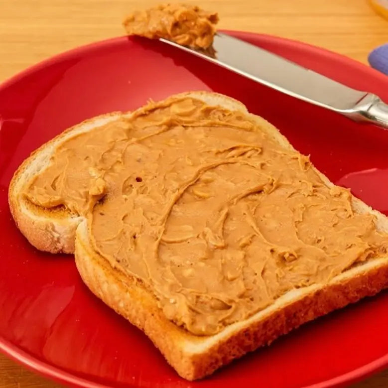Two slices of bread with Sun-Pat Crunchy Peanut Butter on a red plate with a knife.