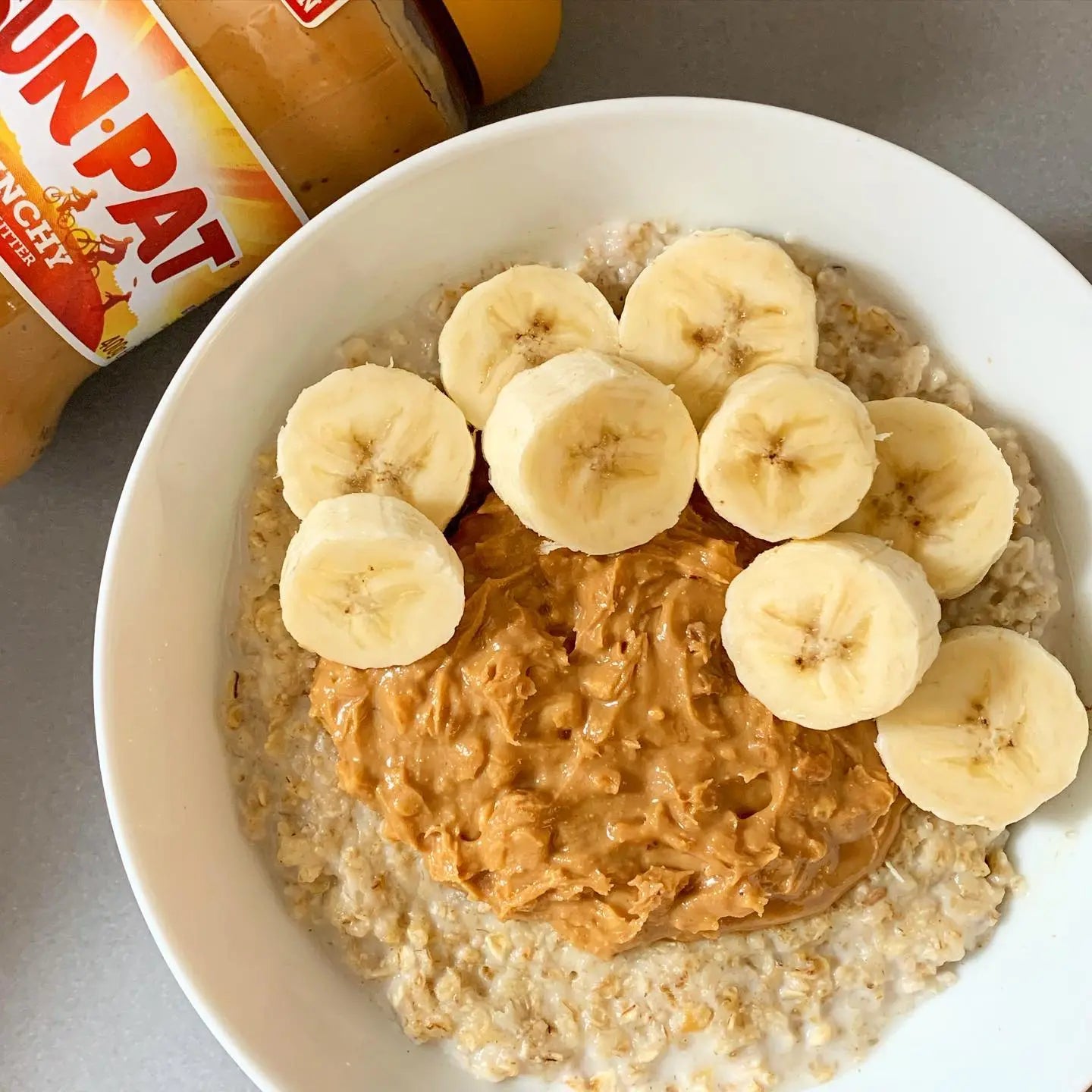 Oatmeal with peanut butter and banana slices in a bowl, Sun-Pat peanut butter jar in the background.