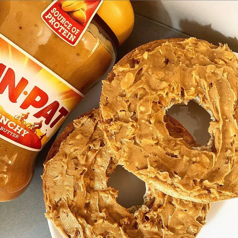 Bagel spread with crunchy peanut butter next to a jar of crunchy peanut butter.
