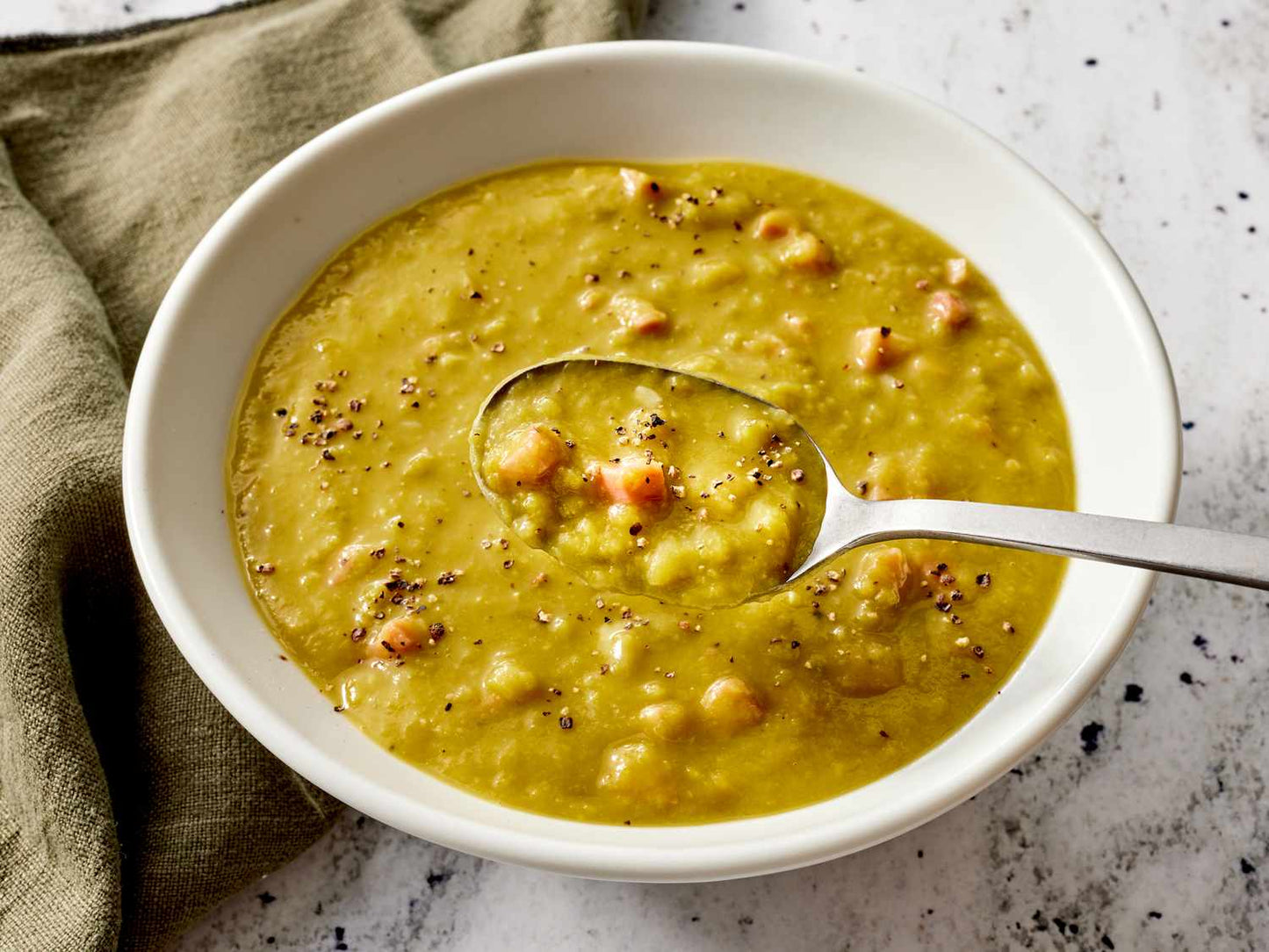 White bowl of split pea soup with a spoon on a textured surface