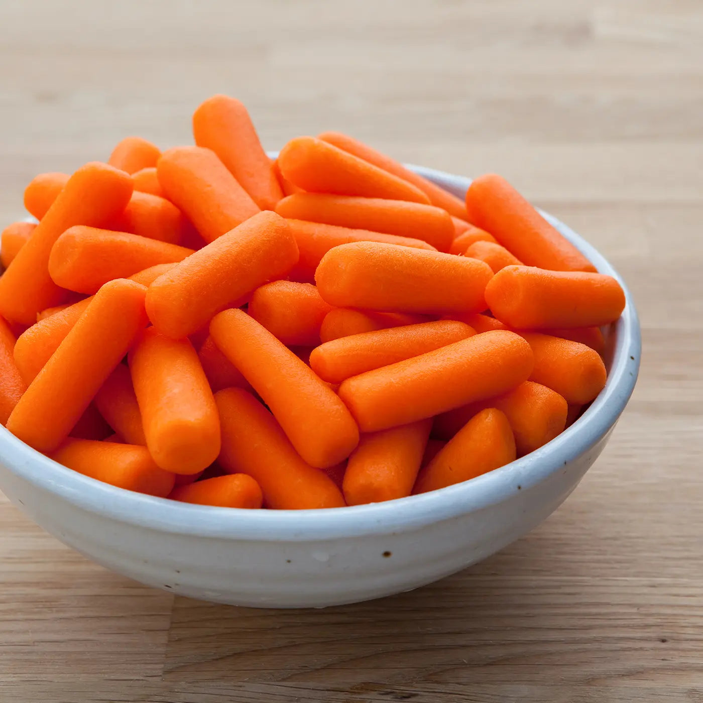 White bowl filled with orange baby carrots on a wooden surface