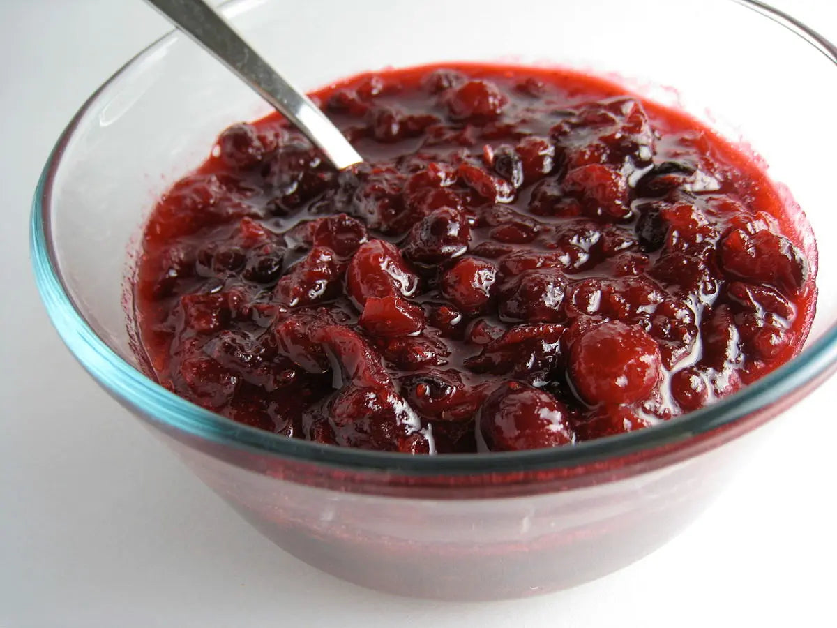 Glass bowl filled with red berry sauce on a white background