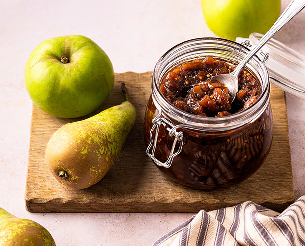 Jar of jam with a spoon, surrounded by apples and pears on a wooden board.