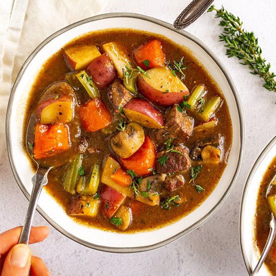 Bowl of vegetable stew with a spoon, garnished with herbs on a light background