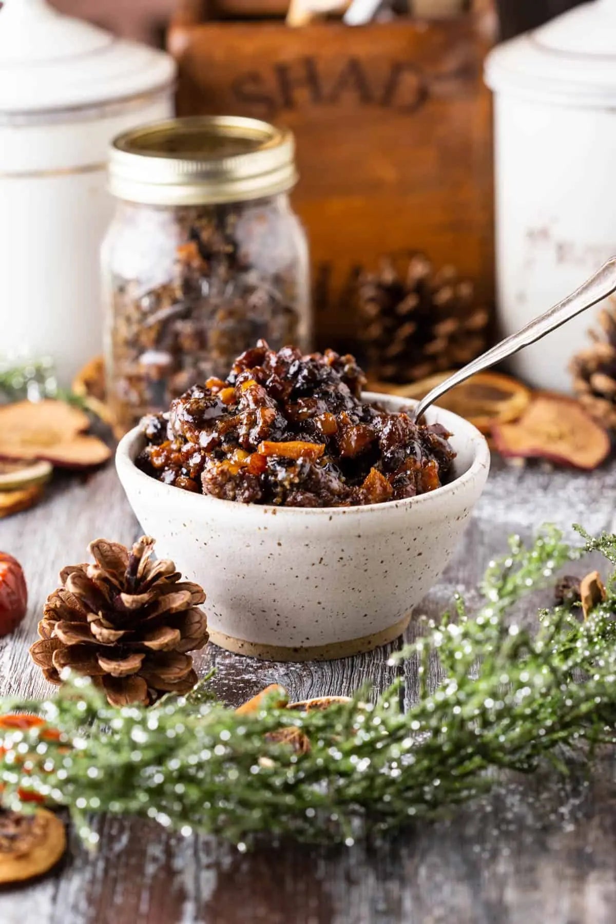 Bowl of dark chocolate truffles with a spoon, surrounded by pine cones and cinnamon sticks on a rustic wooden surface.