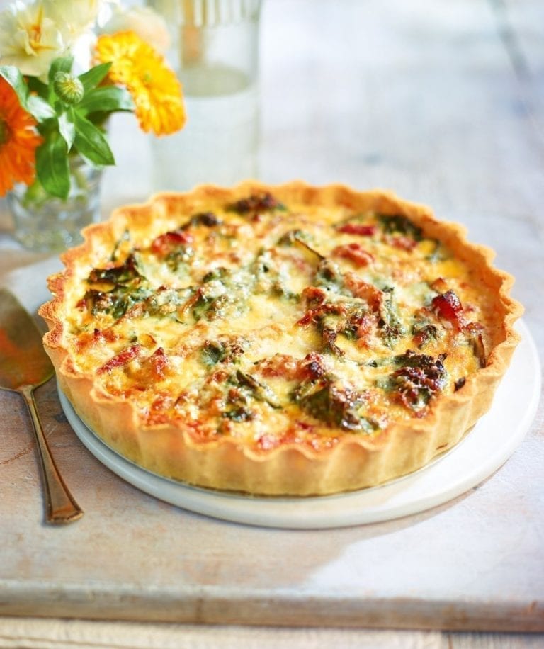 Quiche on a white plate with flowers in the background