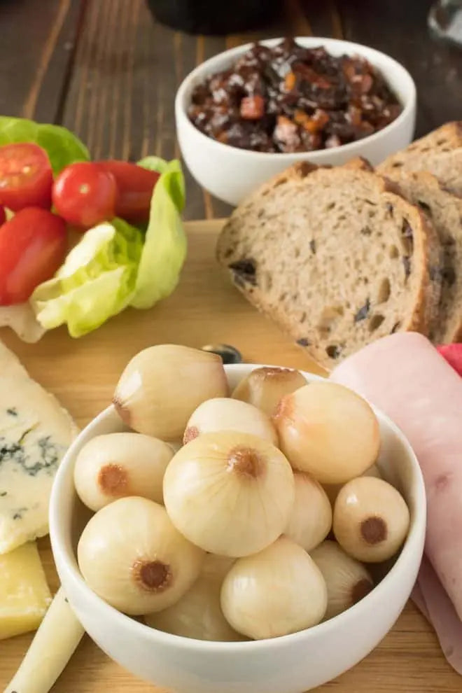 Bowl of onions on a wooden board with bread, tomatoes, and cheese.