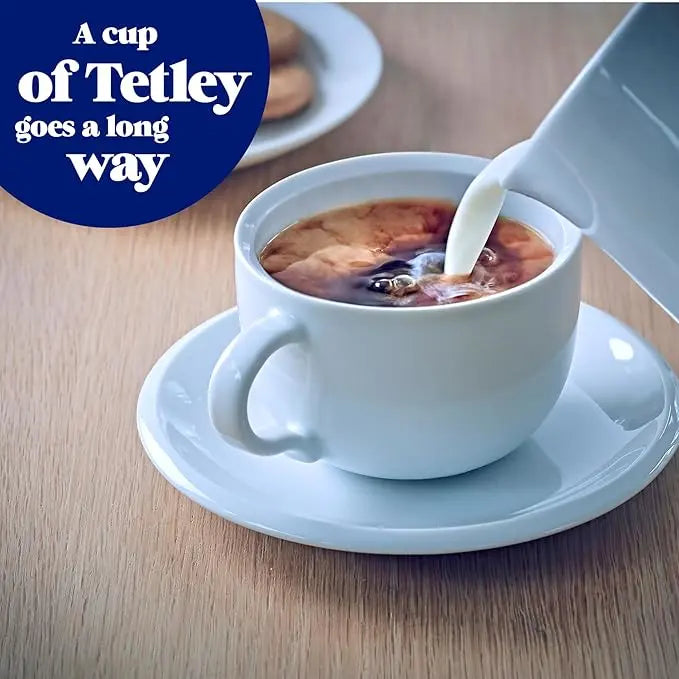White cup of coffee with milk being poured, on a wooden table with 'A cup of Tetley goes a long way' text.
